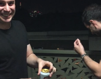 guy in black cracks beer open with head, most spill on his face 