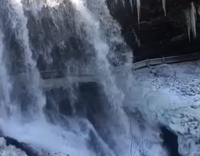 Girl in purple jeans next to waterfall slips on ice and hits rail 
