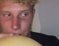 Guy in black clarijs shirt sucking air out of golden balloon