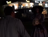 Guy in light blue button up yells at mannequin then prances away and falls into bush