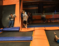 Boy in grey shirt does flip on orange trampoline, falls on head 