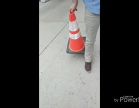 Guy in blue button up and khakis crosses the street and back with orange traffic cone