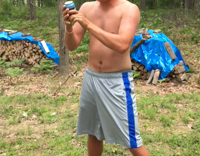 Shirtless guy in grey shorts tries to crack open a beer over his head 