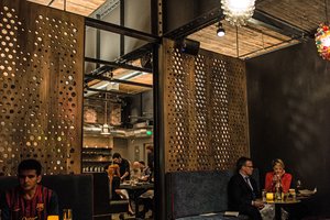 Preview of Mamnoon Restaurant - Image 5: Person, Furniture, Dining Room, Dining, Couch, Dining Table, Wood Screen, Wood, Exposed Structure, Steel, Structure Steel, Light Fixture, Exposed Duct, Brick, Restaurant.