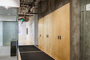 Preview of Undead Labs - Image 3: interior design, commercial space, concrete wall, wood panels, carpet flooring, recessed lighting, ceiling pipes, glass door, modern, hallway, corridor, visible ductwork, steel frame door, minimalist, texture contrast, ambient lighting.