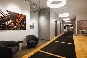 Preview of Undead Labs - Image 7: modern, office, corridor, exposed brick, concrete wall, wood flooring, pendant lighting, recessed lighting, artwork, texture contrast, neutral color palette, black furniture, open space.