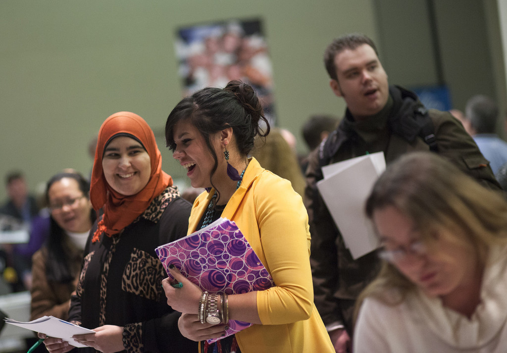 two women, one wearing a hijab scarf, holding notebooks and laughing.