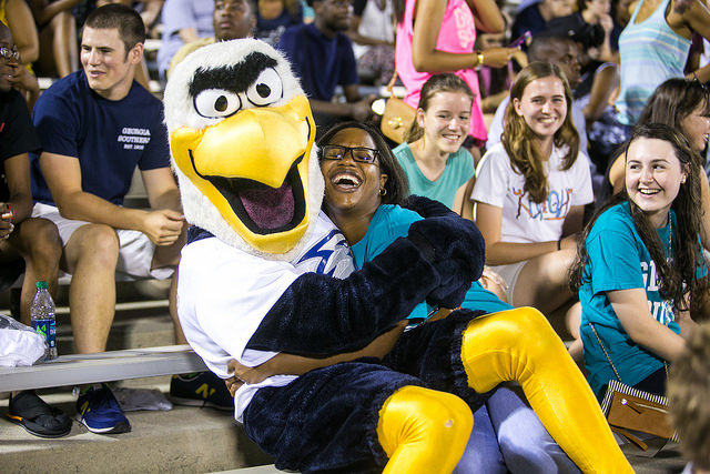 an Eagle mascot sitting on the lap of a woman in bleachers