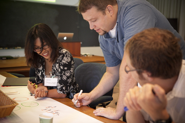 Three students leaning over a sheet of butcher block paper, with markers in their hands