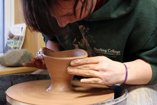 A person at a pottery wheel creating a bowl out of clay