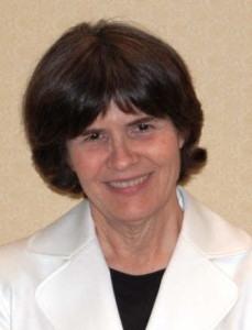 Head-shot photo of a woman with brown hair, smiling into the camera.  She is wearing a white jacket and black shirt.