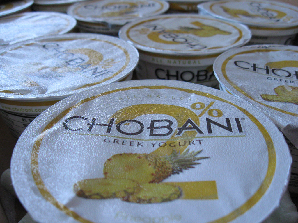 Photo of the lids of the Chobani-brand Greek yogurt containers. The text "Chobani Greek Yogurt" is printed in front of larger text stating 2%, and above a picture of a pineapple.