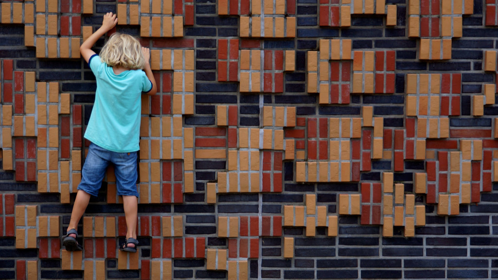 Photo of a child climbing a brightly coloured brick wall.