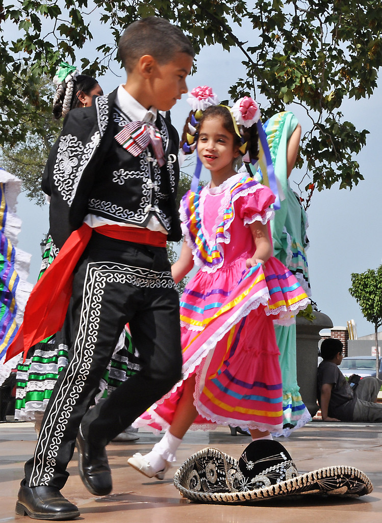 Un niño y una niña mexicanos vestidos con elegantes trajes tradicionales bailan.