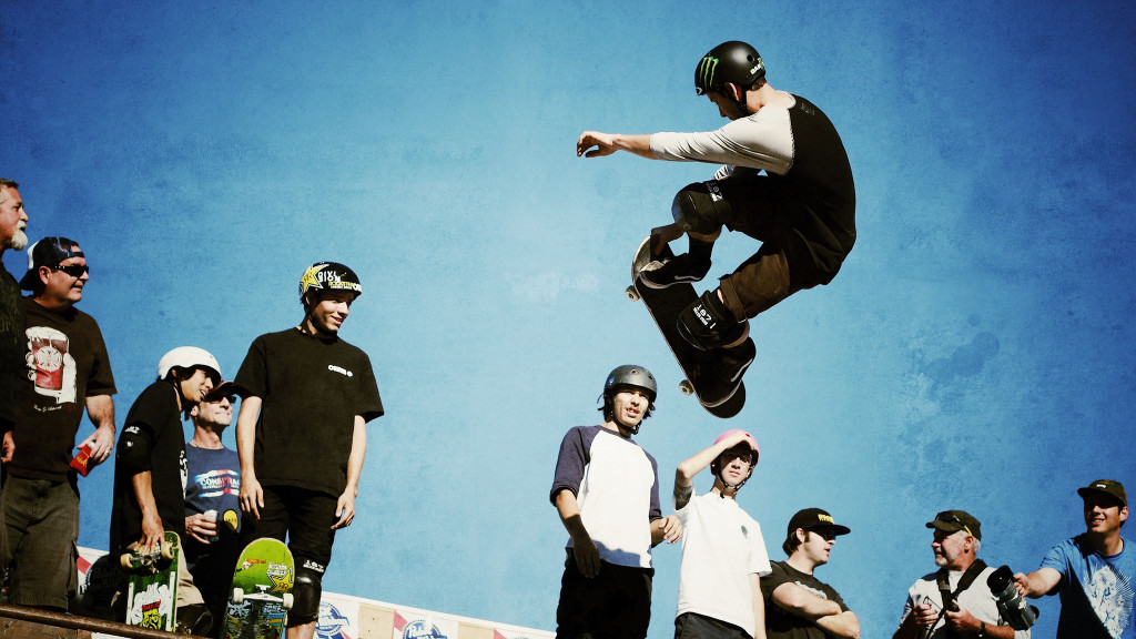 Eine Gruppe von Skateboardern sieht zu, wie ein anderer Skateboarder einen Kunstflug durchführt.