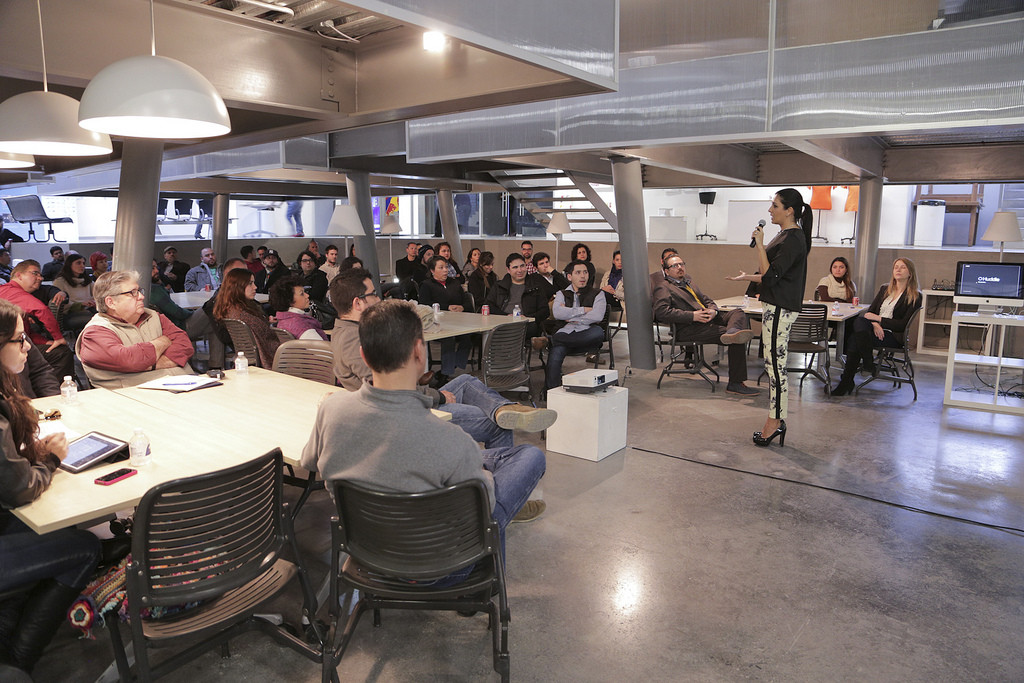 A group of people in a meeting listening to a woman with a microphone.