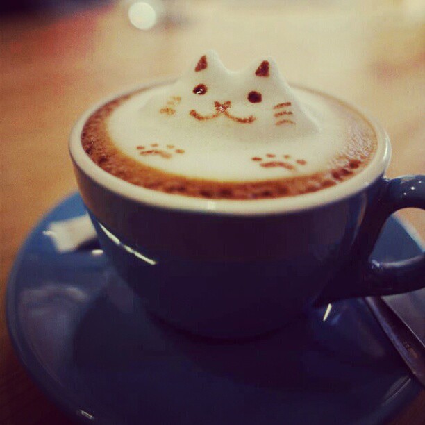 A mug containing a foamy drink. The foam is in the shape of a happy cat.