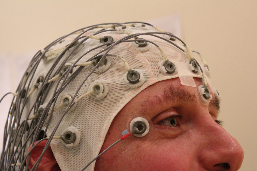 Photo of the upper half of a man's head is shown. He's wearing a mesh fabric cap with multiple electrodes connected to it. The photo title is "Volunteer Duty—Psychological Testing"