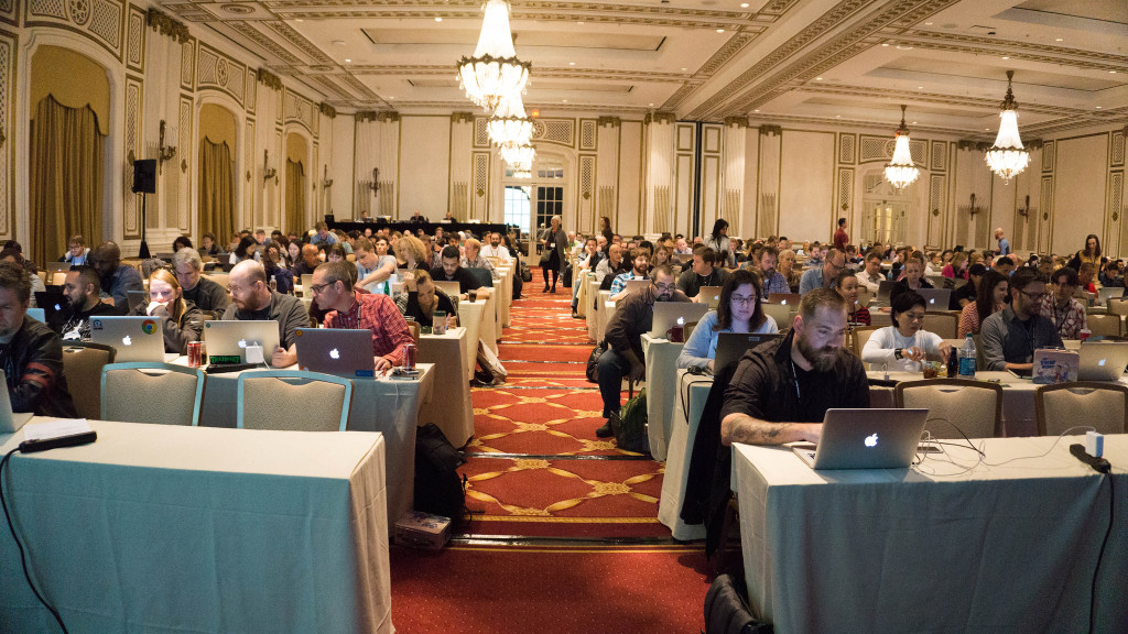 A conference room full of people sitting with laptops at tables.