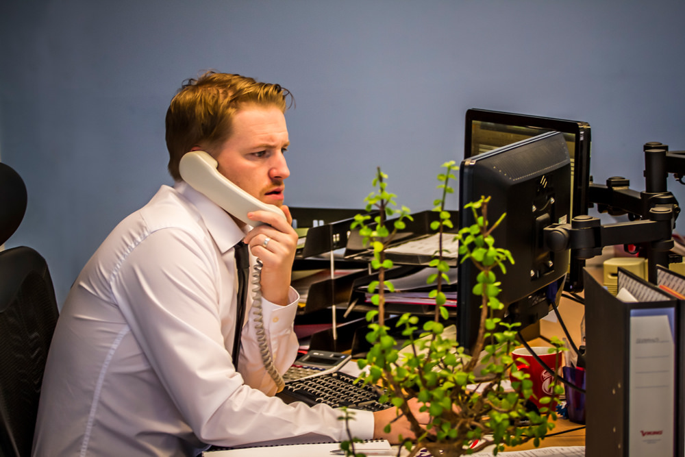 A man in front of a computer talking on the phone.