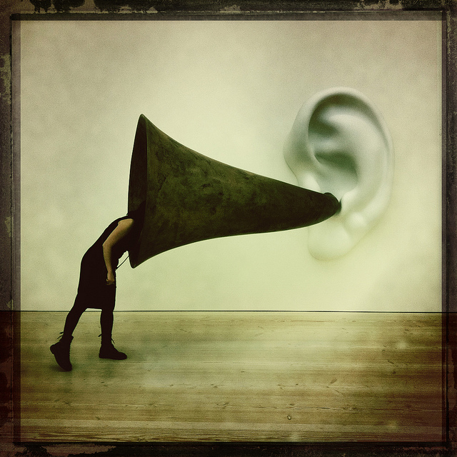 Person with head stuck in large trumpet coming out of ear statue