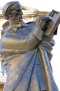 Photo of a bronze statue of a standing man in robes writing on a tablet