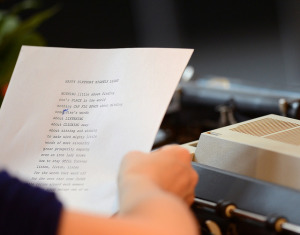 Photo looking over the shoulder of a person holding a piece of paper with a typed poem on it. It has been edited in one spot with handwriting