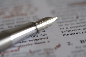 Photo of a fountain pen sitting on top of a printed page. Editing marks have been made in red on the page