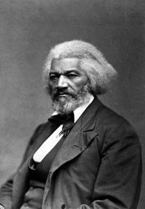 Black and white photograph of Frederick Douglass. He is seated, wearing a suit, appears as an older man, and is looking off to the left of the camera