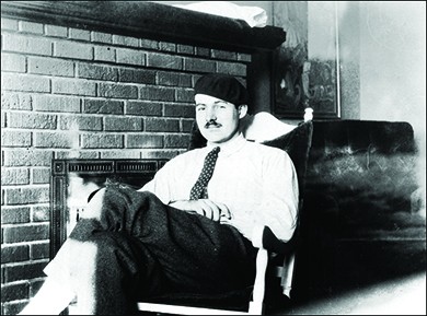 A photograph shows Ernest Hemingway reclining in a chair in front of a fireplace.