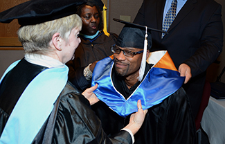 Several people are gathered outdoors wearing caps and gowns in a graduation ceremony.