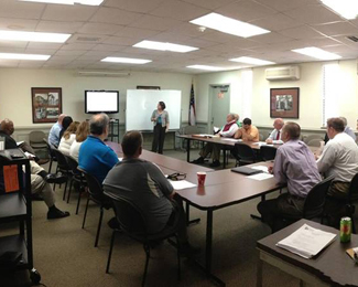 A group of people seated around tables in a meeting room.