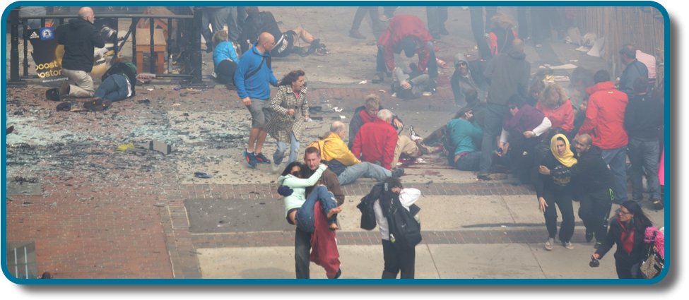 A photograph shows a crowd at the site of the Boston Marathon bombing immediately after it occurred. Debris is scattered on the ground, several people appear to be injured, and several people are helping others.