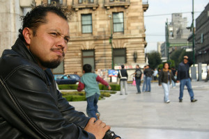 Young man in black jacket looking deep in thought, in foreground of busy street scene