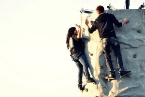 Young woman high-fiving man while nearing the top of a rock climbing wall