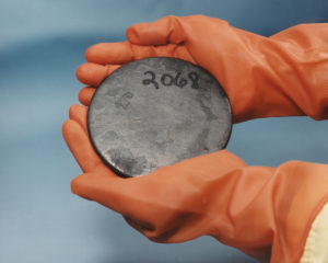 Gloved hands holding a dish of highly enrich uranium metal.