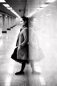 Black and white photograph of a woman leaning against a marble wall. Her reflection is mirrored clearly in the wall.