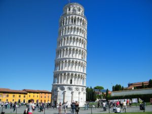 Photo shows the Leaning Tower of Pisa from the nearby courtyard with tourists all around.