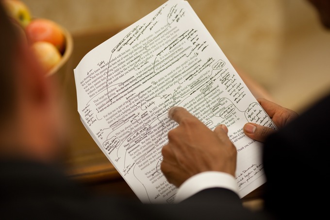 Two men review a copy of a speech with notes written on it.