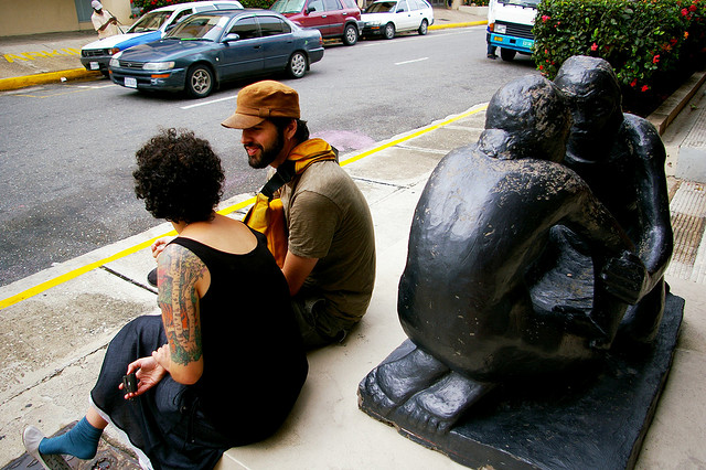 A picture of a man and woman talking while sitting next to a statue.