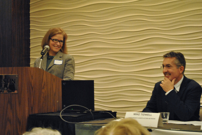 A woman stands at a podium and looks over at another presenter.