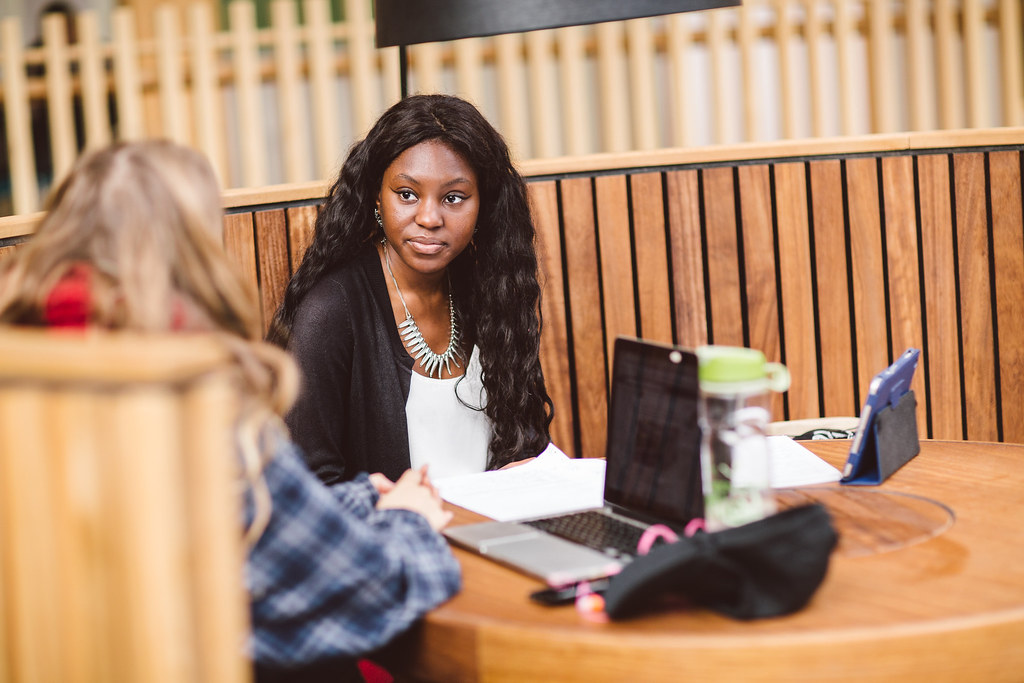 Two students talking around laptops at a table.