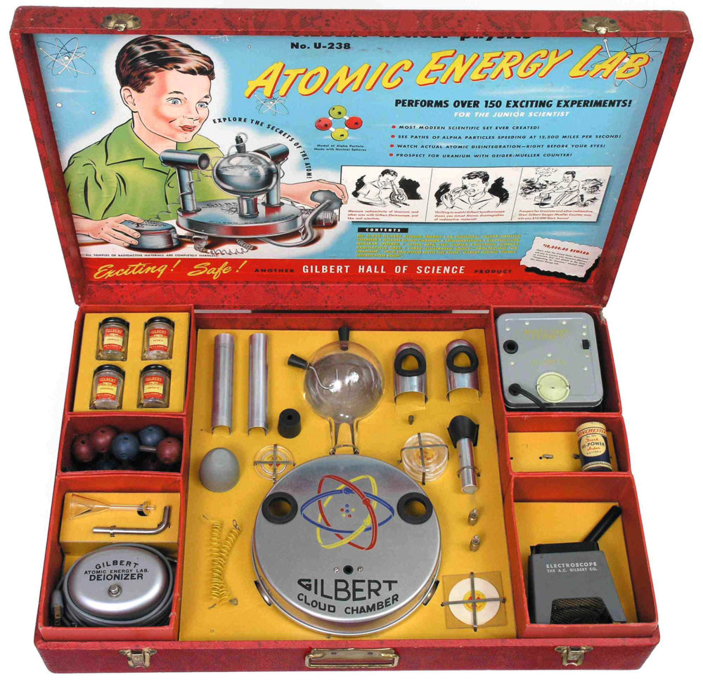 Atomic Energy Lab kit, packaged in a red briefcase with a boy excitedly playing with the pieces in a picture on one side of the case, while the other is filled with the needed parts.