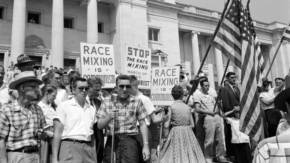 White protesters outside of the Arkansas Capitol holding signs like "mixing race is communism" and American flags.