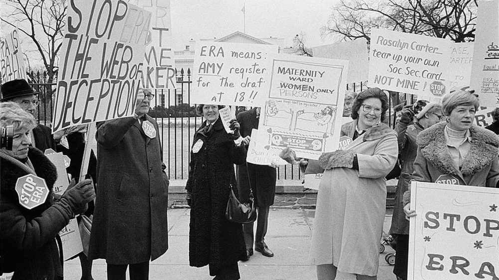 Protestors against the ERA carry signs like "stop the web of deception" and "ERA means AMY register for the draft at 18" and "Rosalyn Carter--tear up your own Soc Sec Card, not mine!"