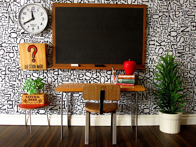 Miniature scene of a desk, chalkboard, plant, wall clock, and other classroom materials