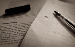 Photo of a textbook on left, overlapped by a piece of notebook paper on the right, with an uncapped pen laying across both