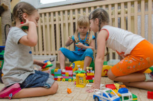 Three young girls build cars and trains with plastic toy blocks. 