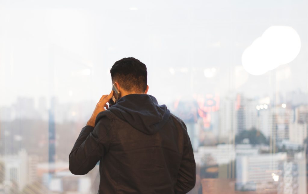 Photograph of a man standing with his back to the camera. He is talking on a cell phone.