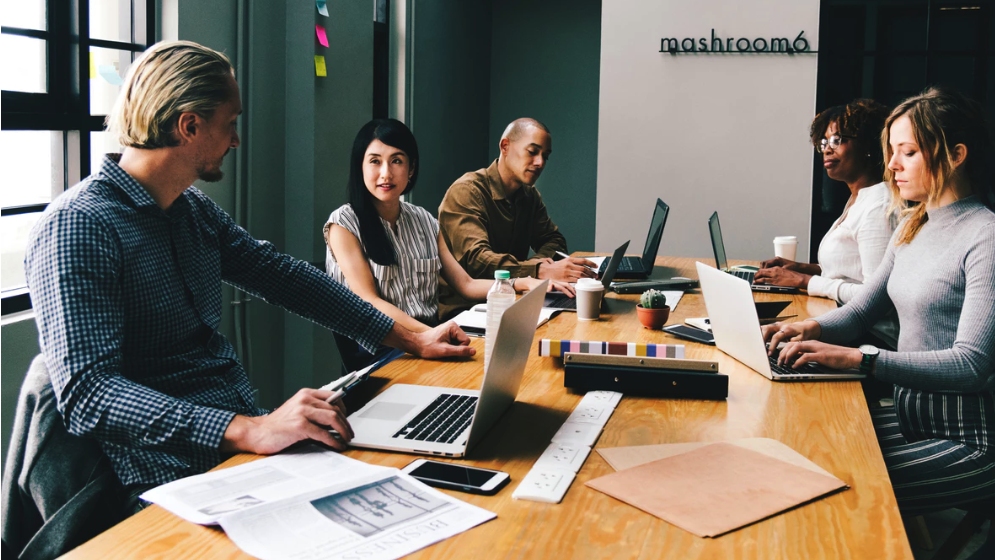 Photograph of five individuals sitting around an office table. All five are wearing business attire.